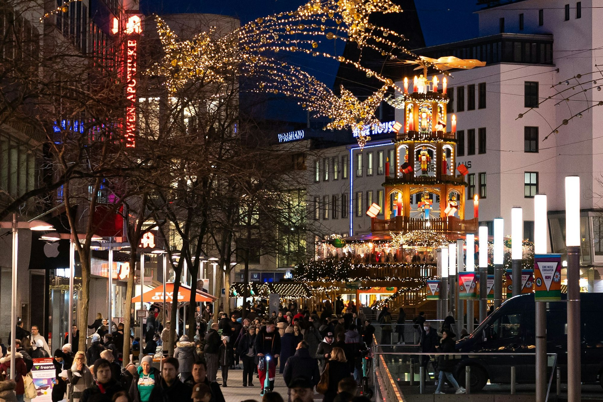 Passanten laufen 2022 durch die Fußgängerzone in der Innenstadt von Hannover. Im Hintergrund steht eine Weihnachtspyramide am Kröpcke, einem zentralen Platz in der Innenstadt.