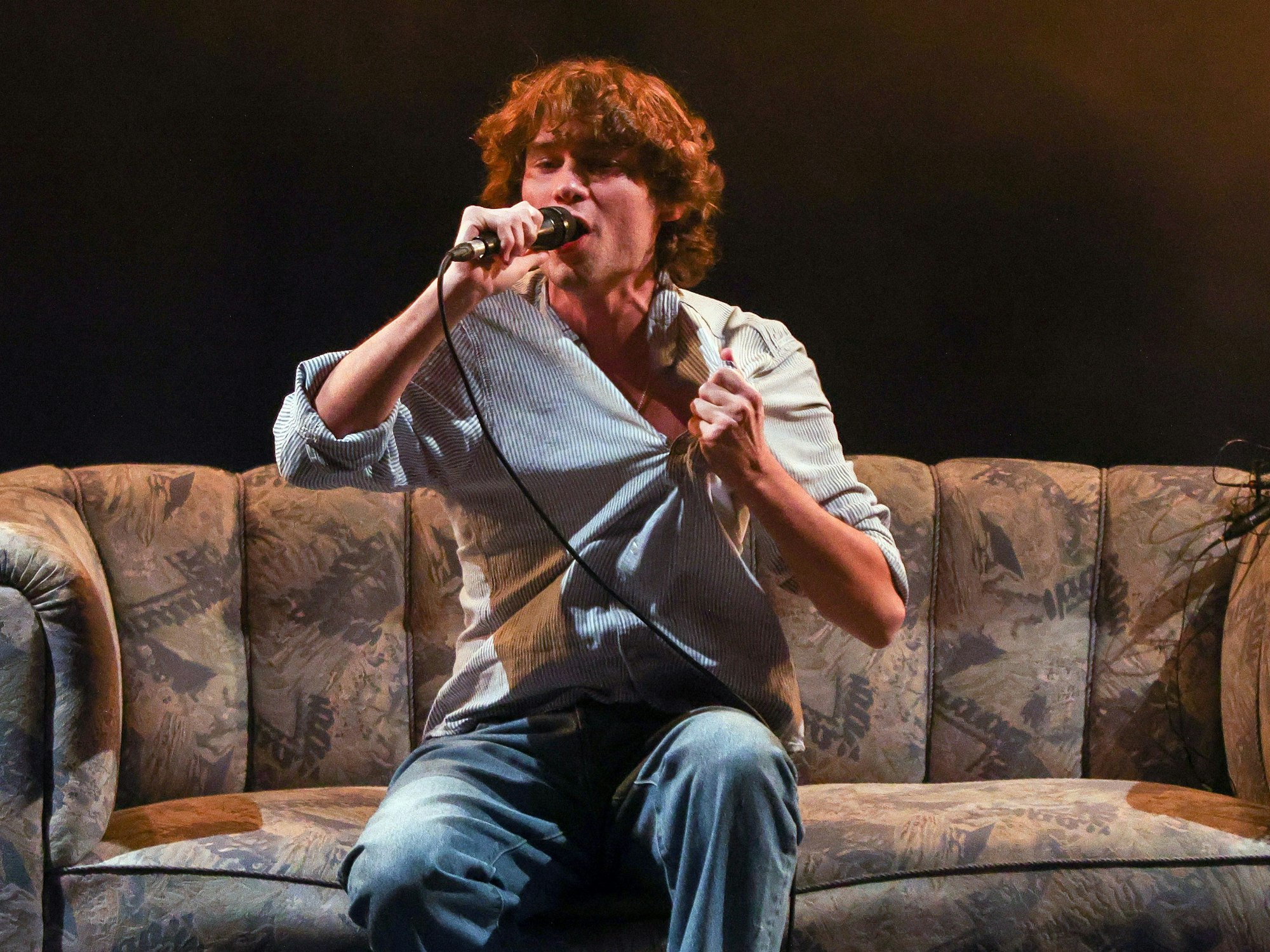 Frontsänger Jeremias Heimbach singt auf einem Sofa bei einem Konzert der Band JEREMIAS.