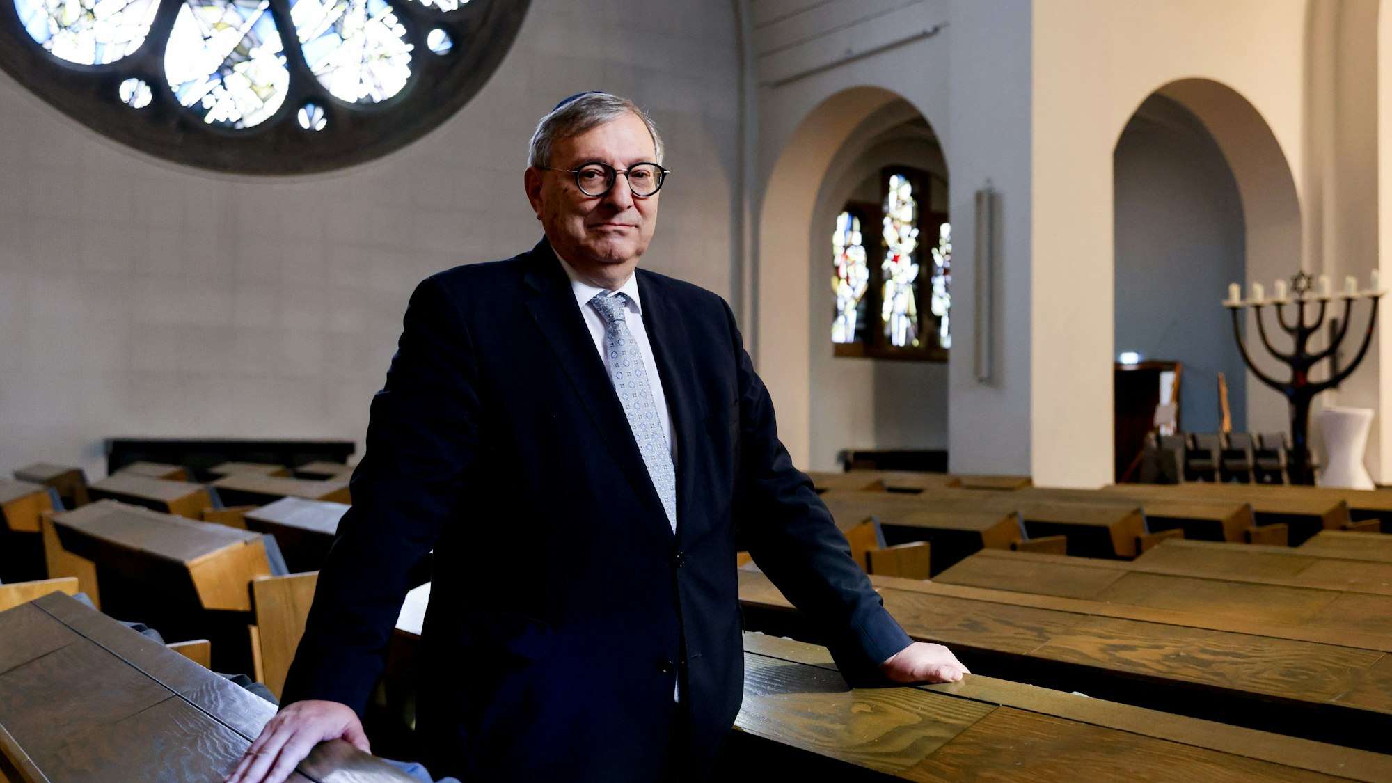 Abraham Lehrer steht in einer Sitzreihe der Kölner Synagoge und schaut in die Kamera.