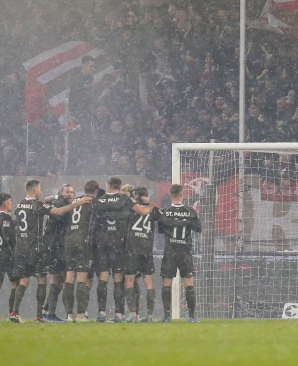 Die Spieler vom FC St. Pauli jubeln nach dem Tor zum 2:0 während Torhüter Daniel Heuer Fernandes vom HSV die Szenerie verfolgt.