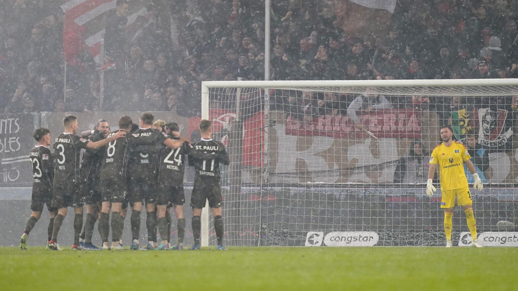 Die Spieler vom FC St. Pauli jubeln nach dem Tor zum 2:0 während Torhüter Daniel Heuer Fernandes vom HSV die Szenerie verfolgt.