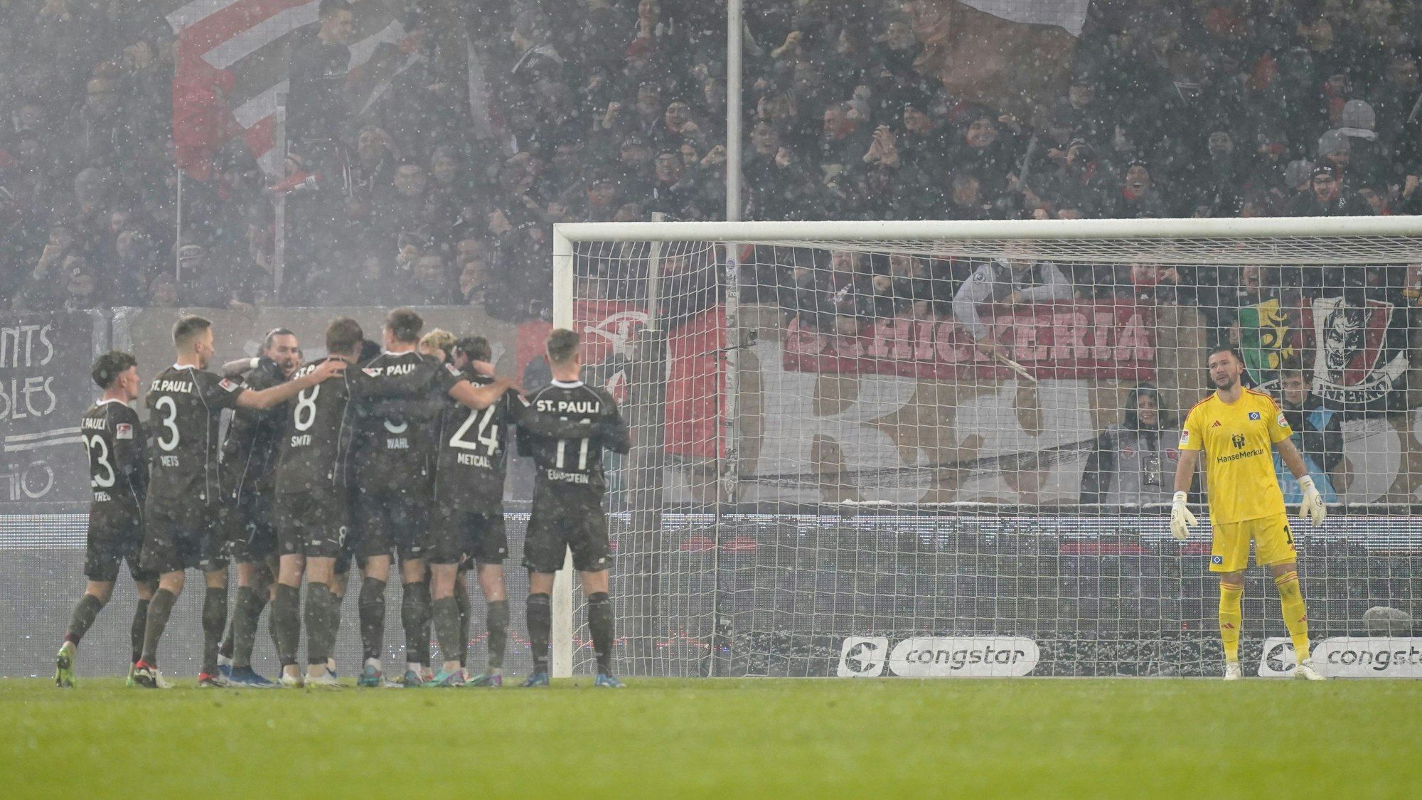 Die Spieler vom FC St. Pauli jubeln nach dem Tor zum 2:0 während Torhüter Daniel Heuer Fernandes vom HSV die Szenerie verfolgt.