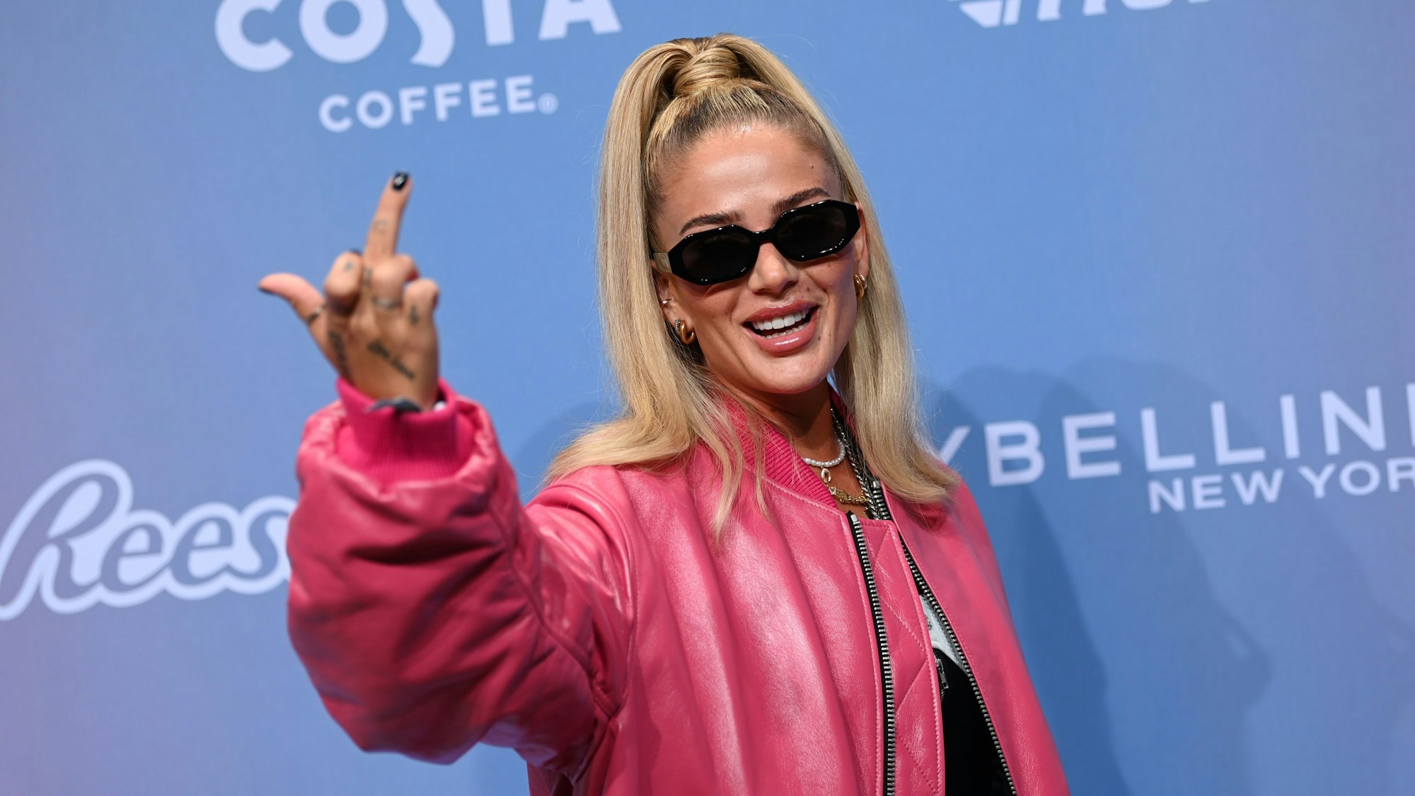 Rapperin Loredana zeigt lächelnd den Mittelfinger und trägt eine Sonnenbrille