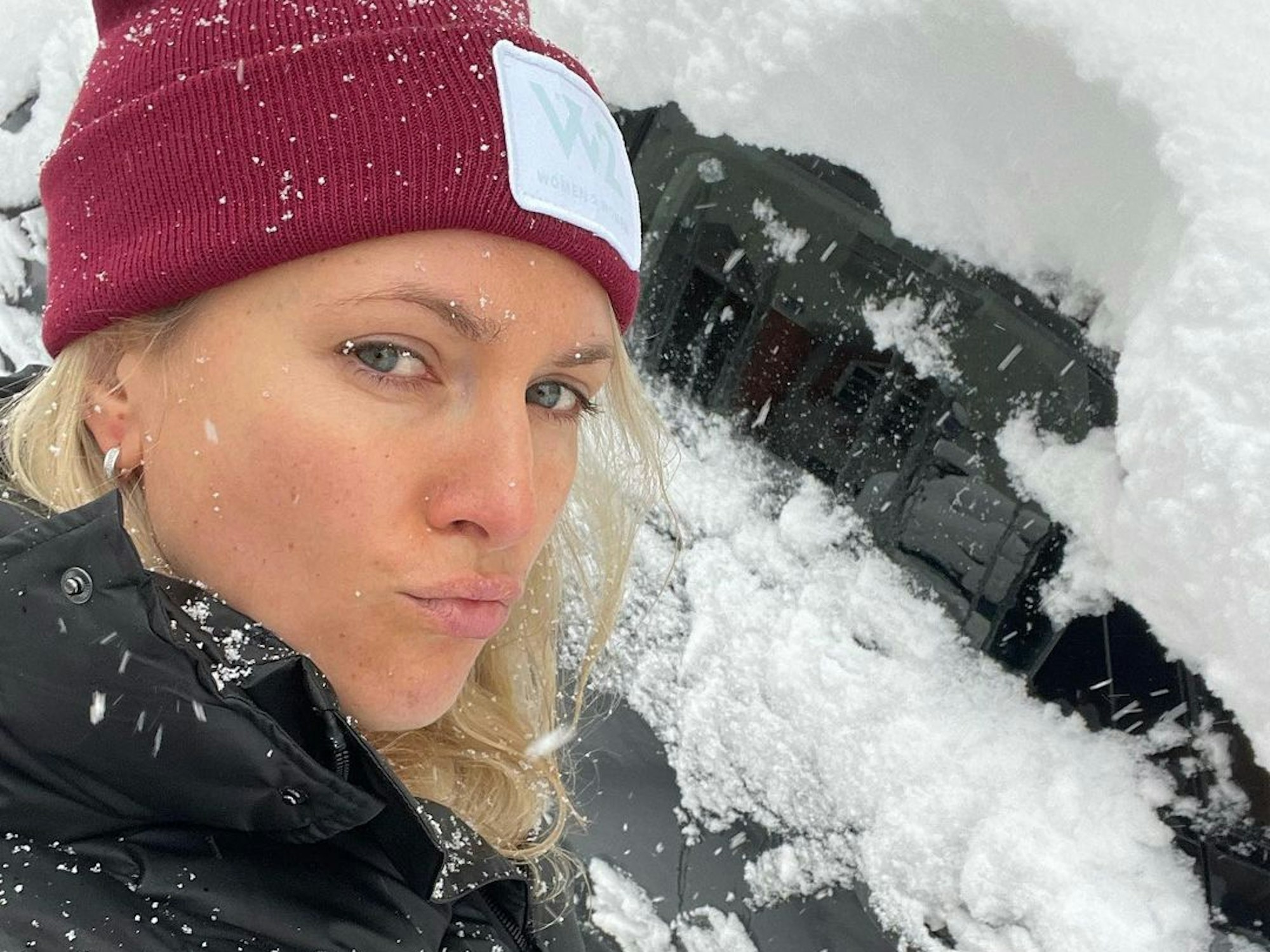 Ruth Hofmann mit Mütze vor ihrem eingeschneiten Auto.