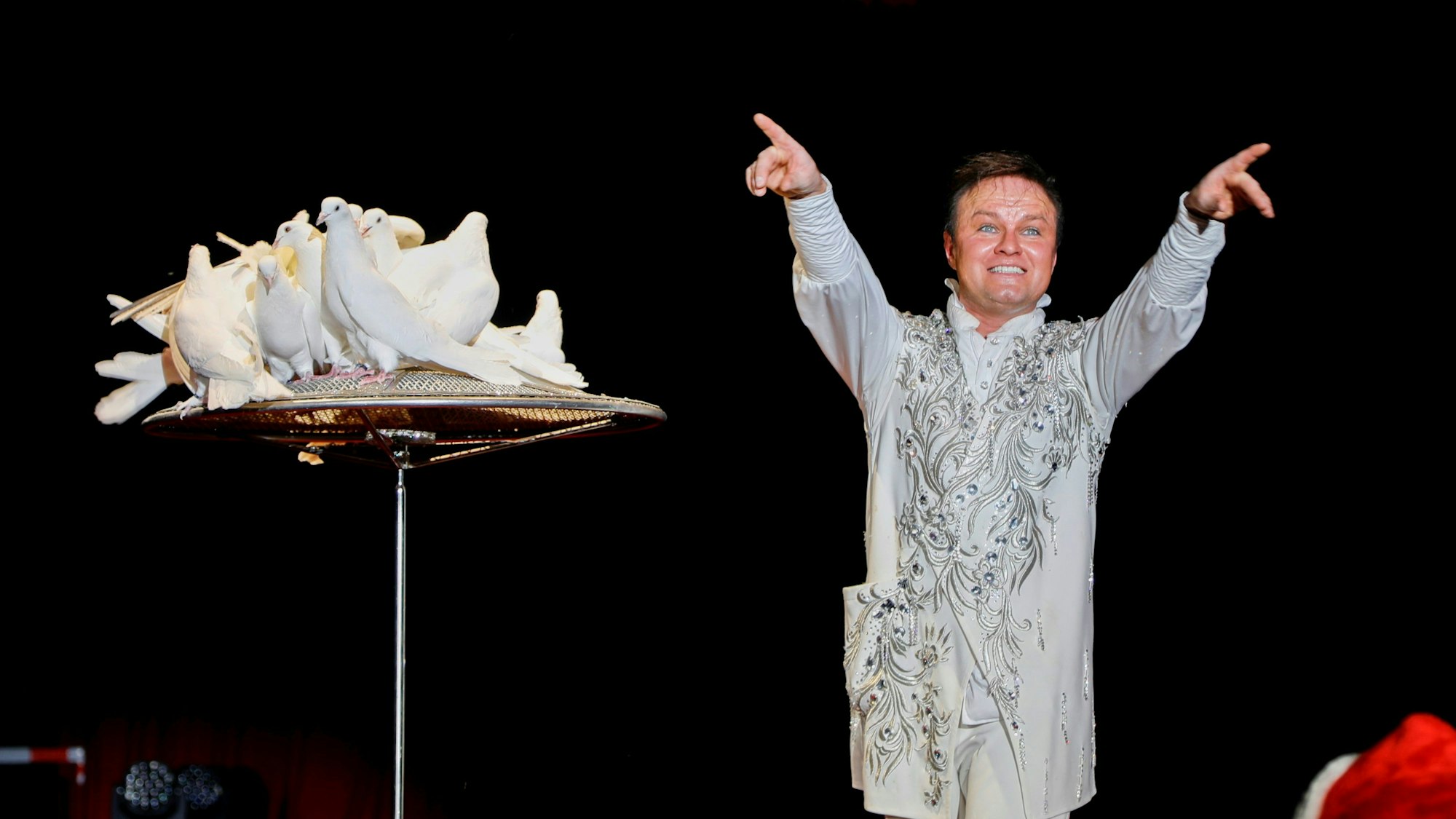 Tierdompteuer Andrej Fjodorow steht in der Manege. Neben ihm sitzen mehrere weiße Tauben.