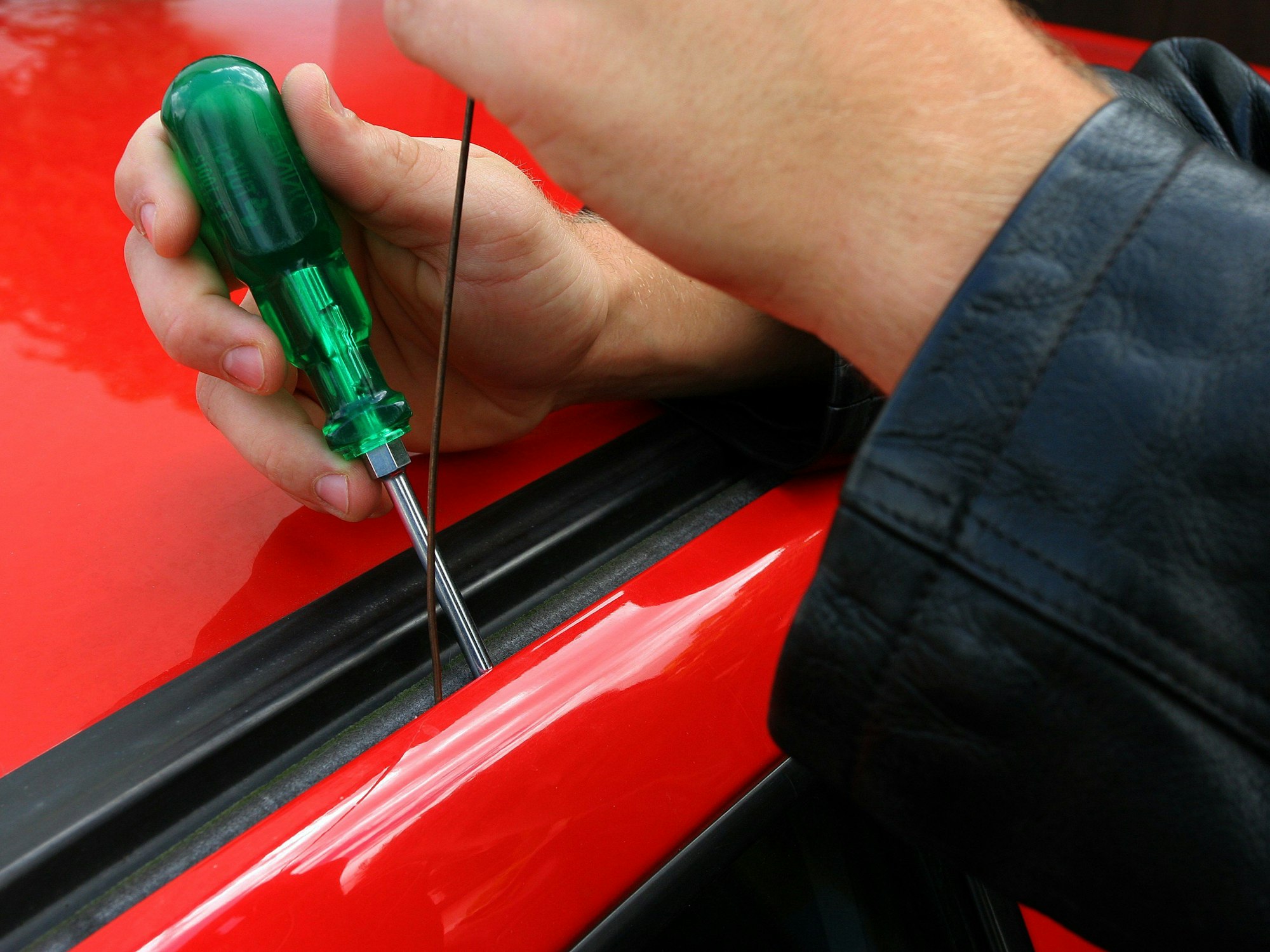Eine Person hat einen Schraubenzieher zwischen Autodach und -tür gesteckt, um sie zu öffnen.