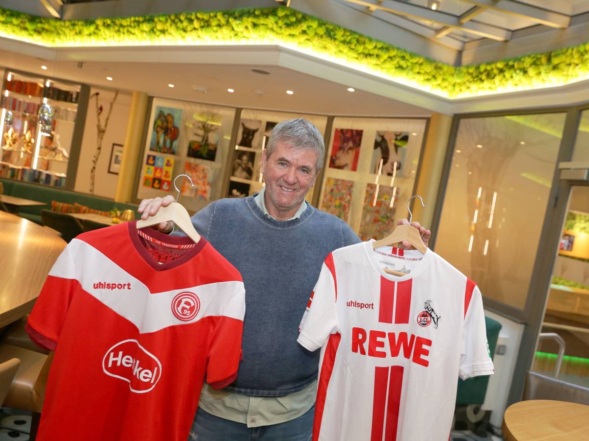 Friedhelm Funkel hält zwei Trikots von Fortuna Düsseldorf und dem 1. FC Köln in die Kamera.