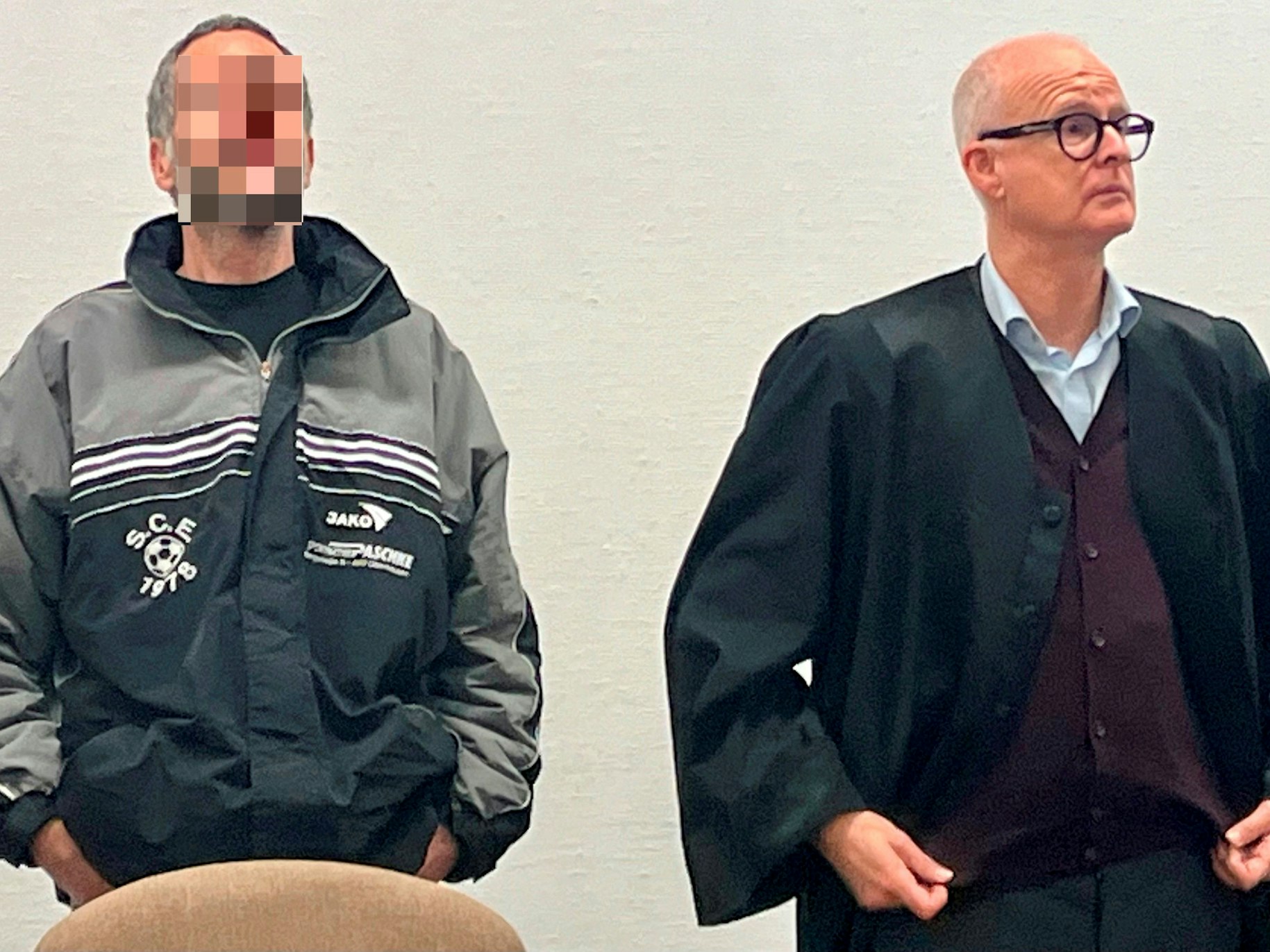 Der Angeklagte und sein Anwalt stehen im Gerichtssaal nebeneinander.
