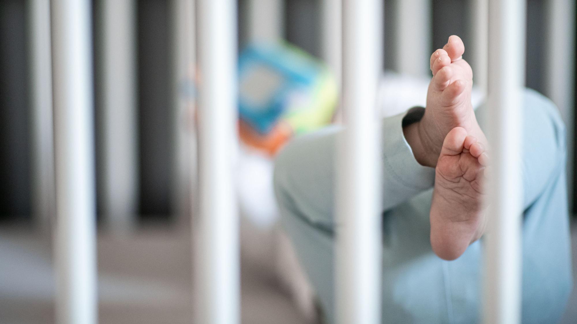 Die Füße eines Babys sind in einem Kinderbett zu sehen.