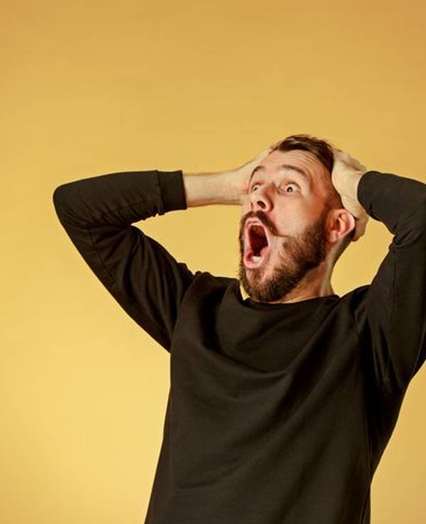 Portrait of young man with shocked facial expression over orange studio background
