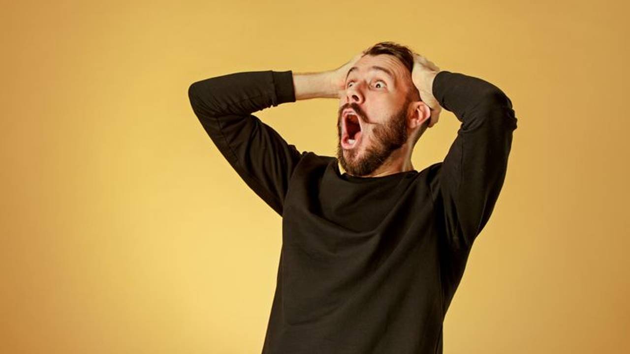 Portrait of young man with shocked facial expression over orange studio background