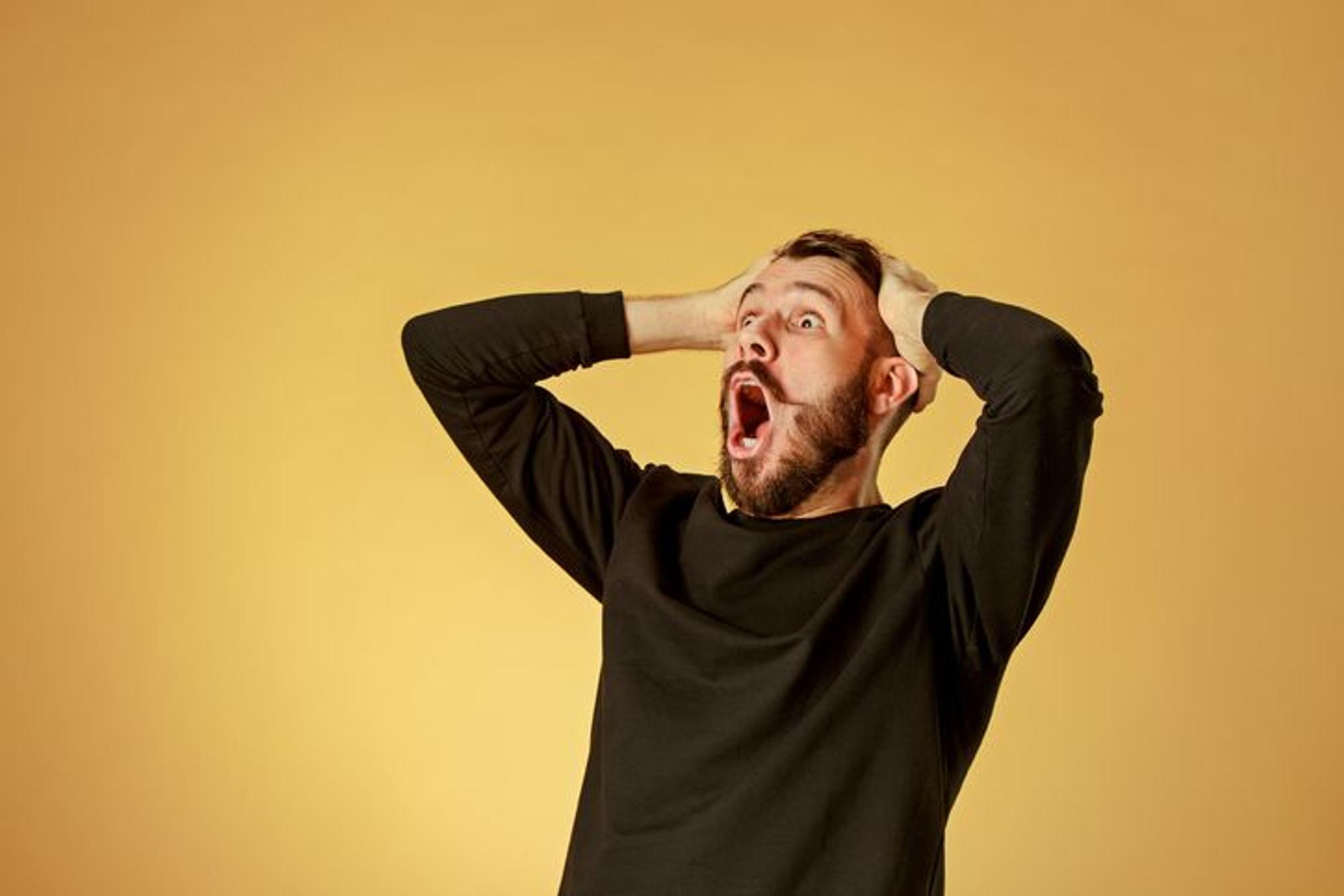 Portrait of young man with shocked facial expression over orange studio background