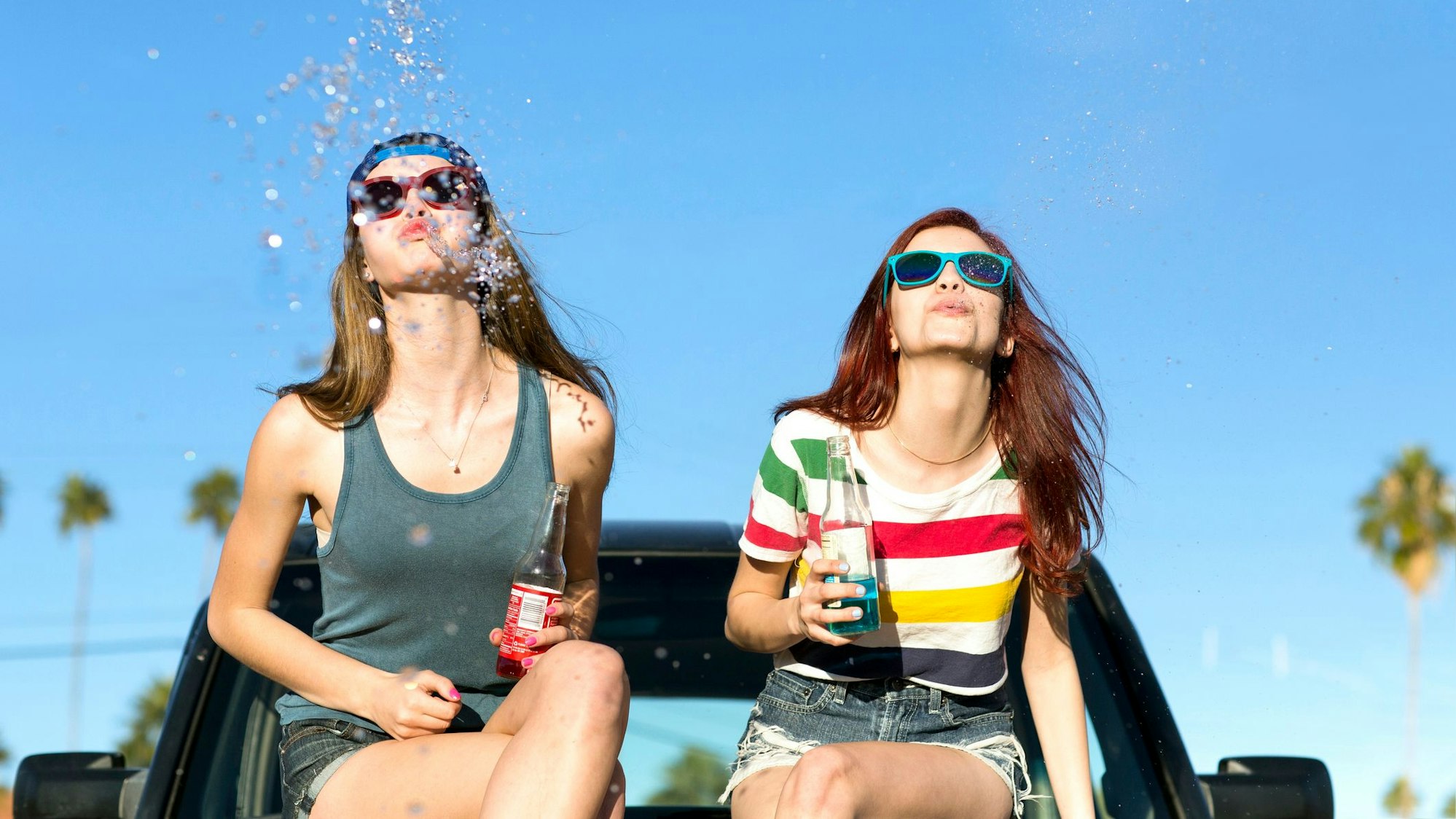 Zwei Teenagerin sitzen auf einem Auto und spuken um die Wette.