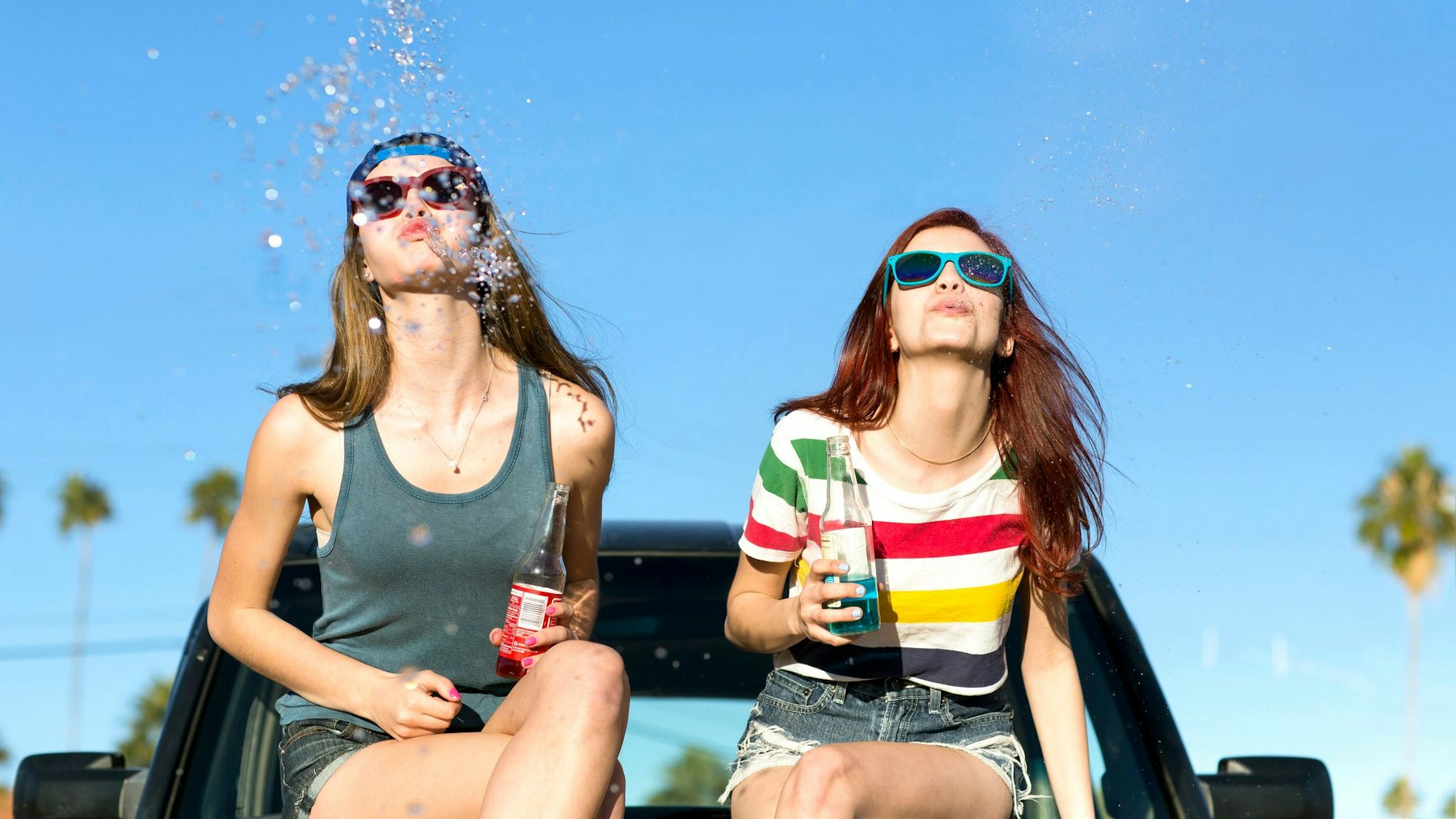 Zwei Teenagerin sitzen auf einem Auto und spuken um die Wette.