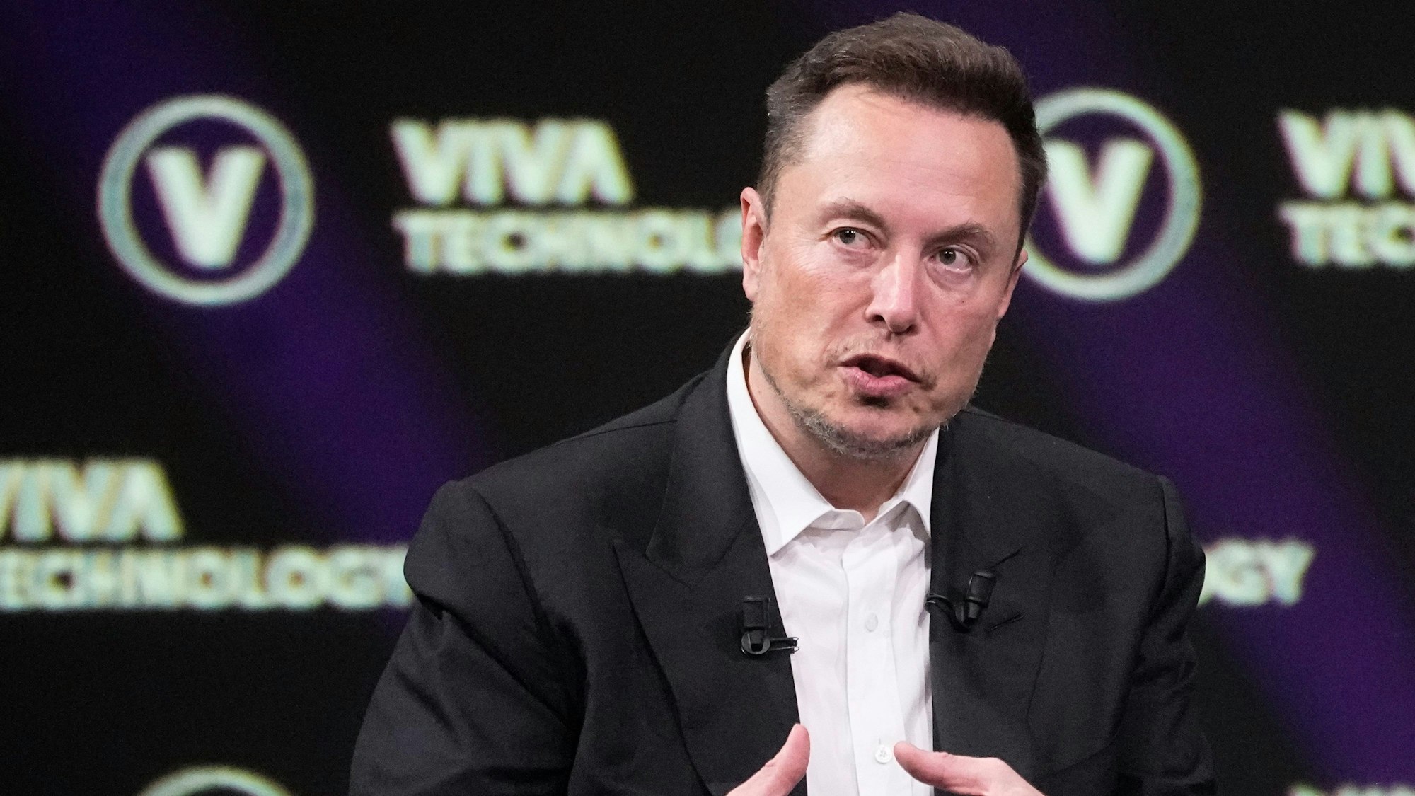 Elon Musk im Anzug, er spricht auf einem Podium während einer Veranstaltung in Paris.