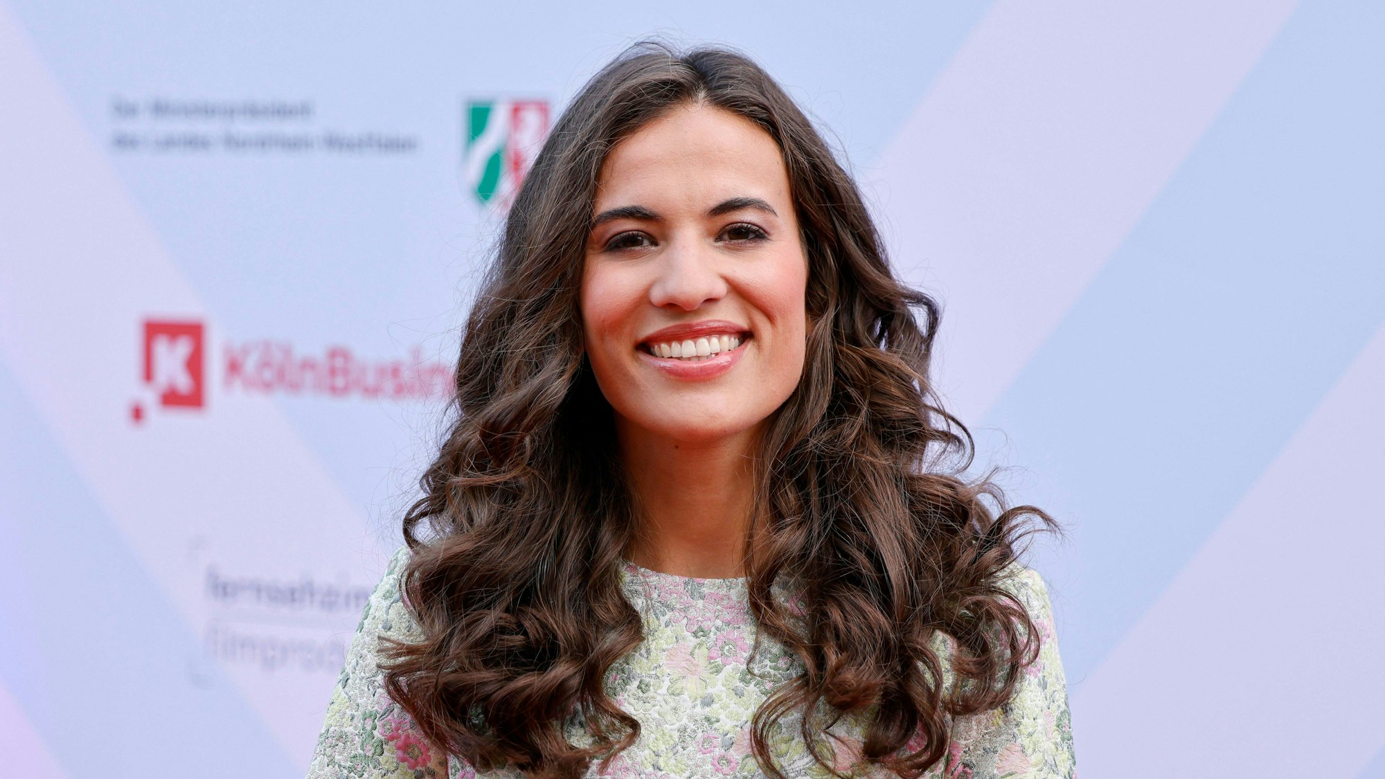 Moderatorin Mona Ameziane auf einem roten Teppich in Köln fotografiert, sie lacht in die Kamera.