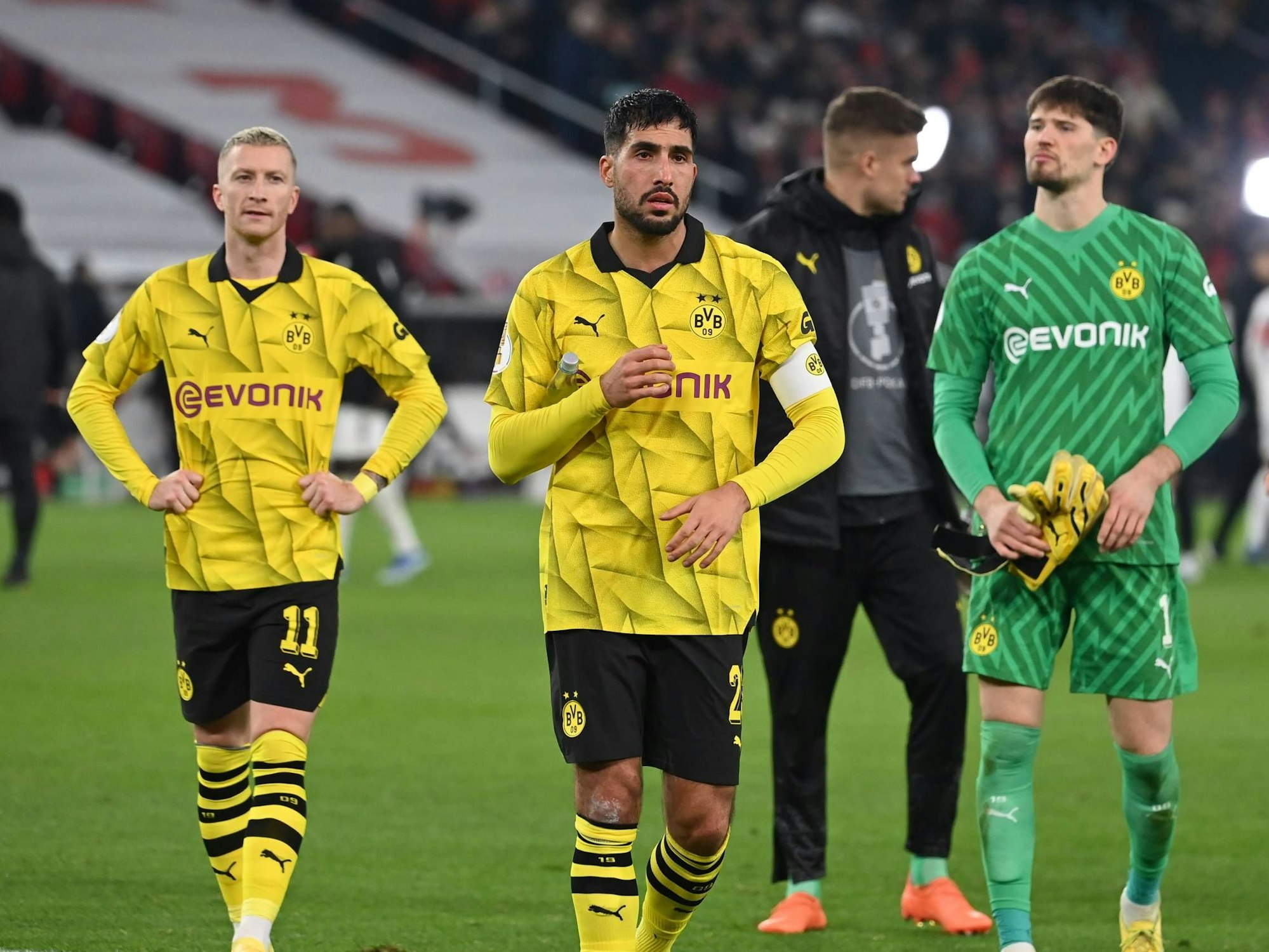 Marco Reus, Emre Can und Gregor Kobel laufen enttäuscht über den Rasen.