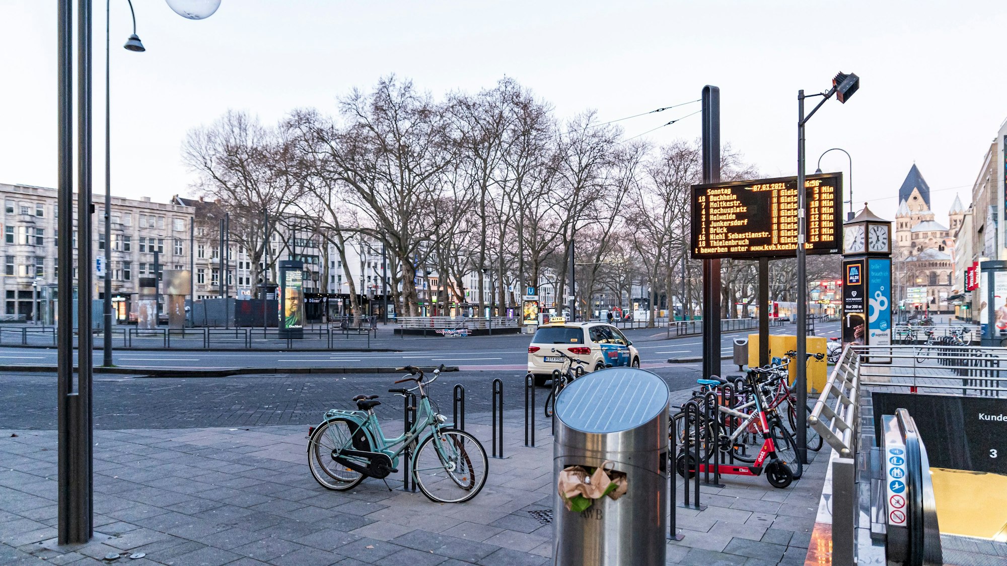 Ein Taxi steht am Kölner Neumarkt, im Vordergrund sind einige Fahrräder zu sehen.