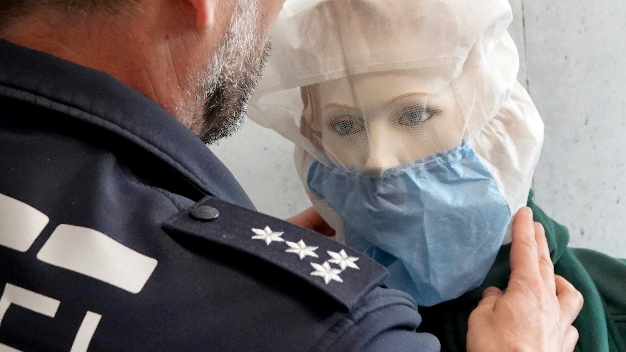 Ein Pressesprecher der Polizei demonstriert die Anwendung einer Spuckschutzhaube an einer Puppe.