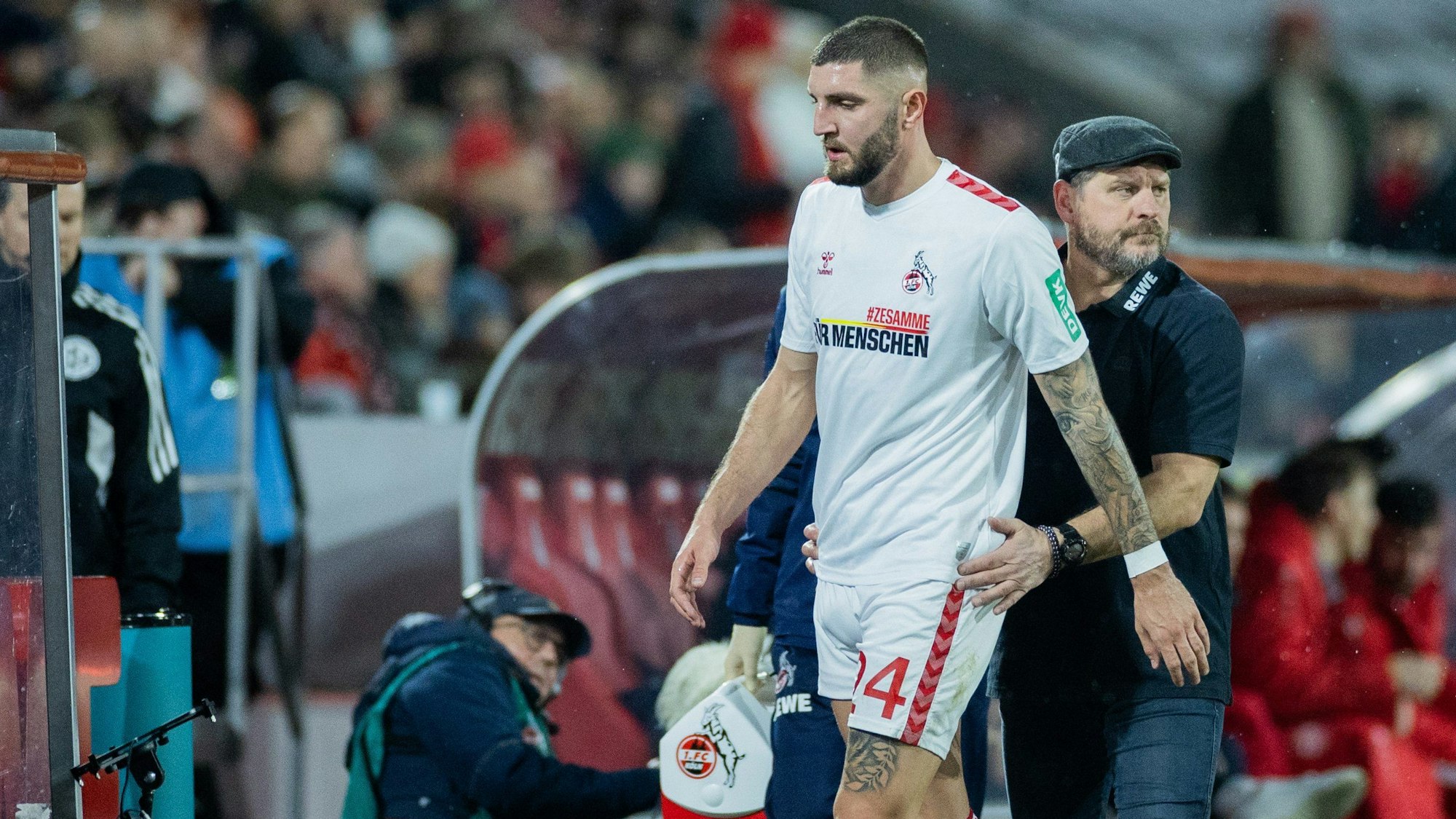 Kölns Jeff Chabot muss verletzt ausgewechselt werden und geht an Trainer Steffen Baumgart (r) vorbei.