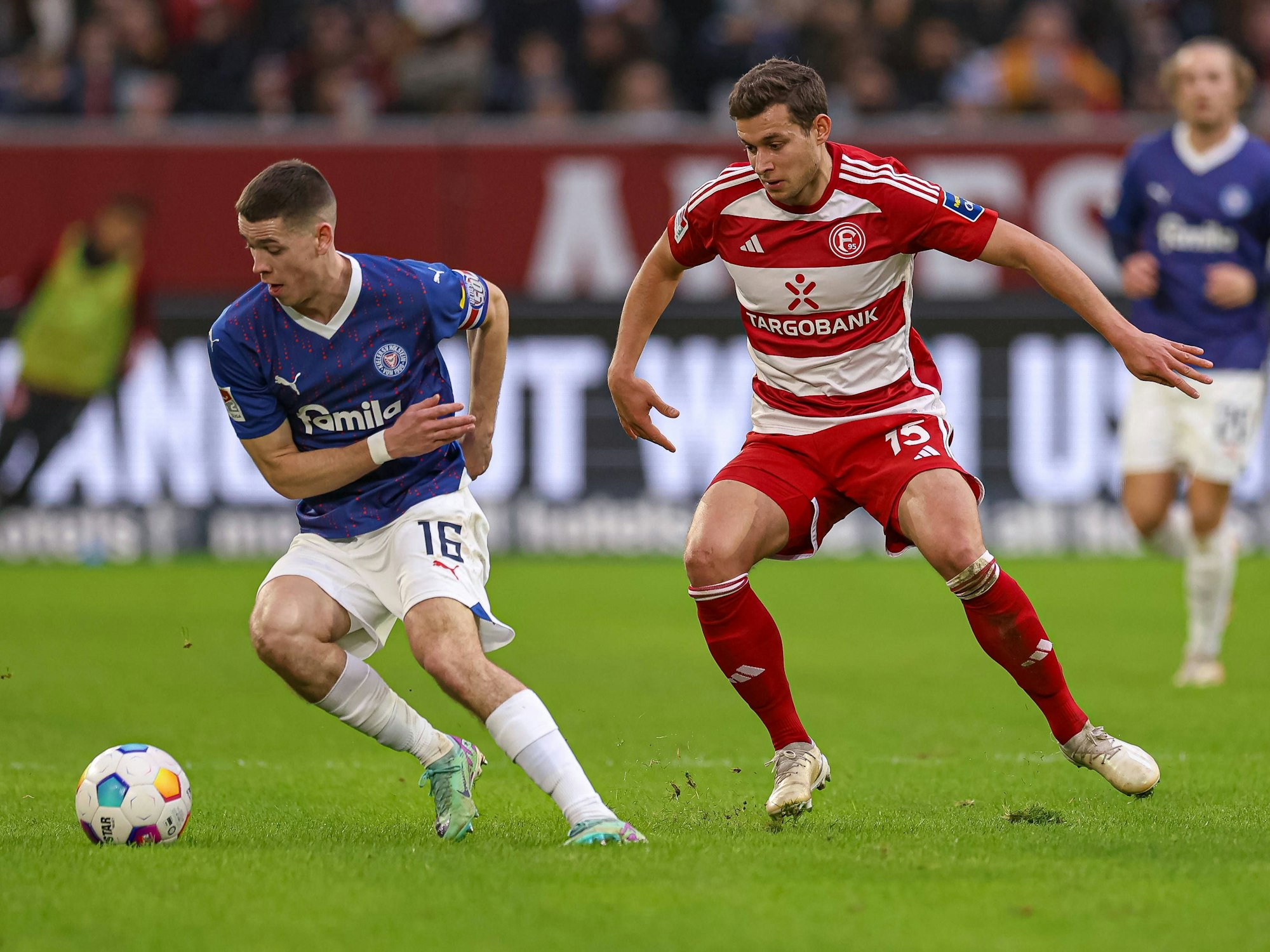 Holstein Kiels Philipp Sander führt den Ball, Fortuna Düsseldorfs Tim Oberdorf steht daneben.