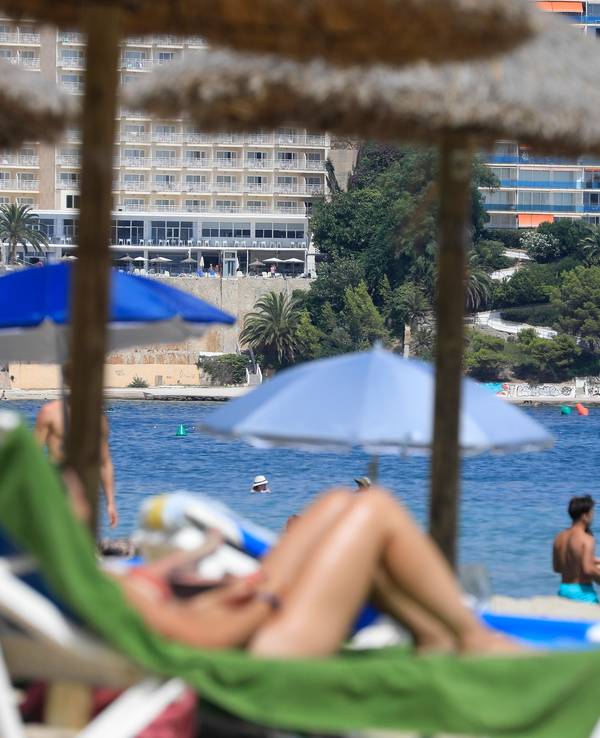 Menschen liegen auf Strandliegen und schwimmen im Meer.