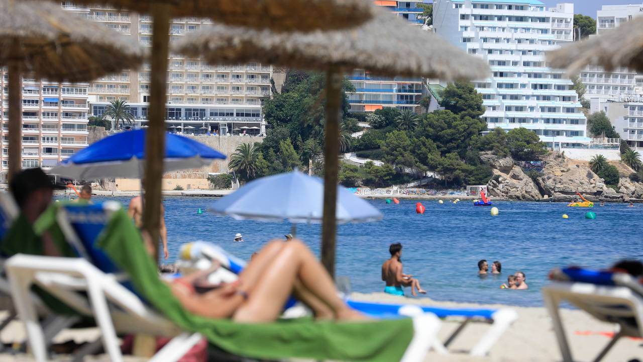 Menschen liegen auf Strandliegen und schwimmen im Meer.