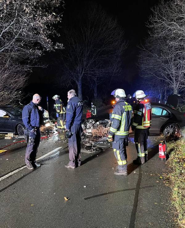 Unfallstelle auf einer dunklen Landstraße, mehrere Personen stehen rund um die zerstörten Autos.