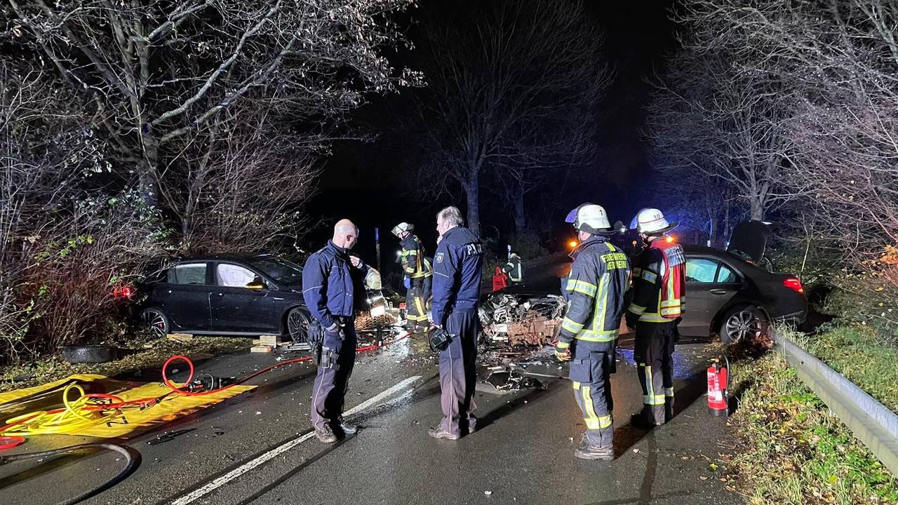 Unfallstelle auf einer dunklen Landstraße, mehrere Personen stehen rund um die zerstörten Autos.
