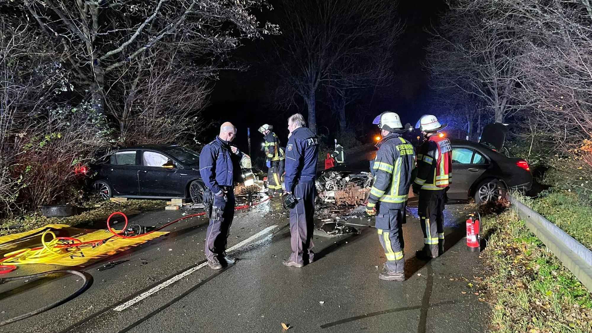 Unfallstelle auf einer dunklen Landstraße, mehrere Personen stehen rund um die zerstörten Autos.