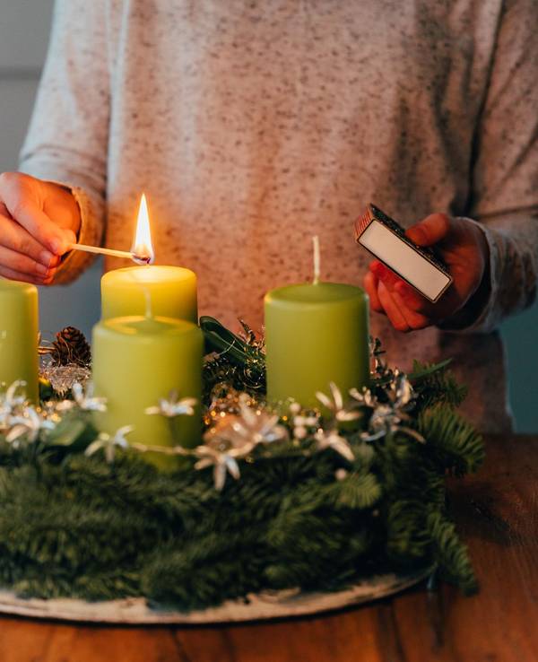 Eine Frau zündet Kerzen am Adventskranz an.