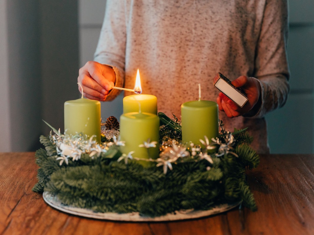 Eine Frau zündet Kerzen am Adventskranz an.