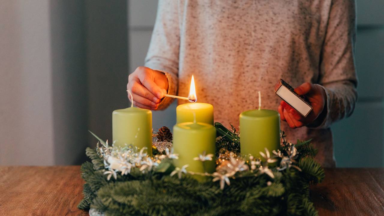 Eine Frau zündet Kerzen am Adventskranz an.