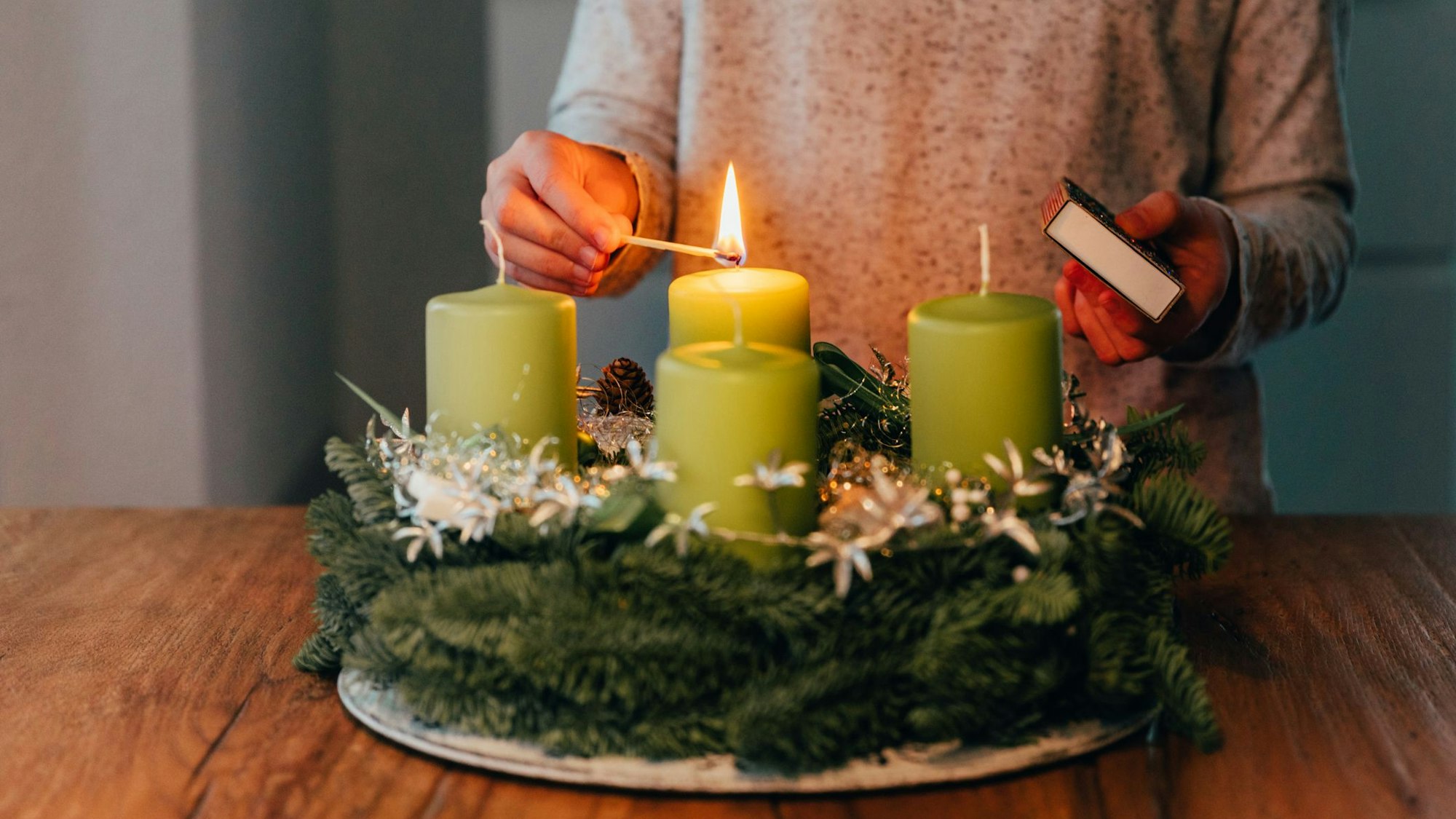 Eine Frau zündet Kerzen am Adventskranz an.