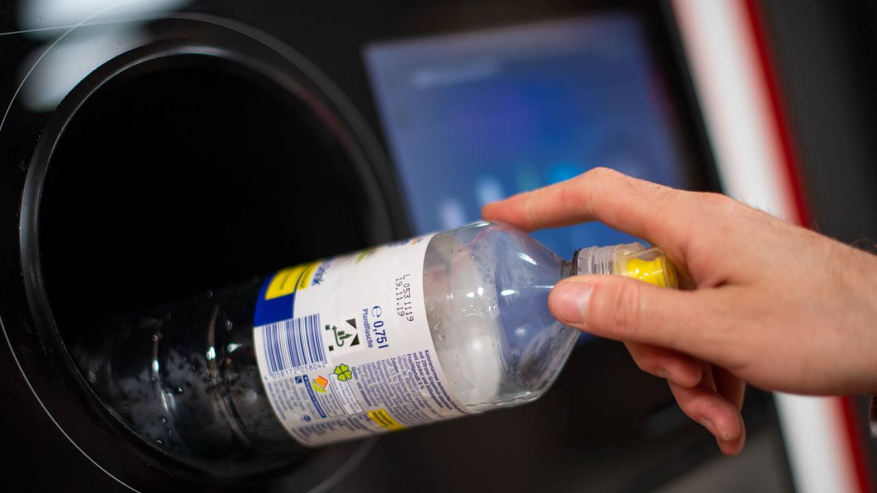 Eine Person steckt eine Pfandflasche in einen Pfandflaschenautomaten.