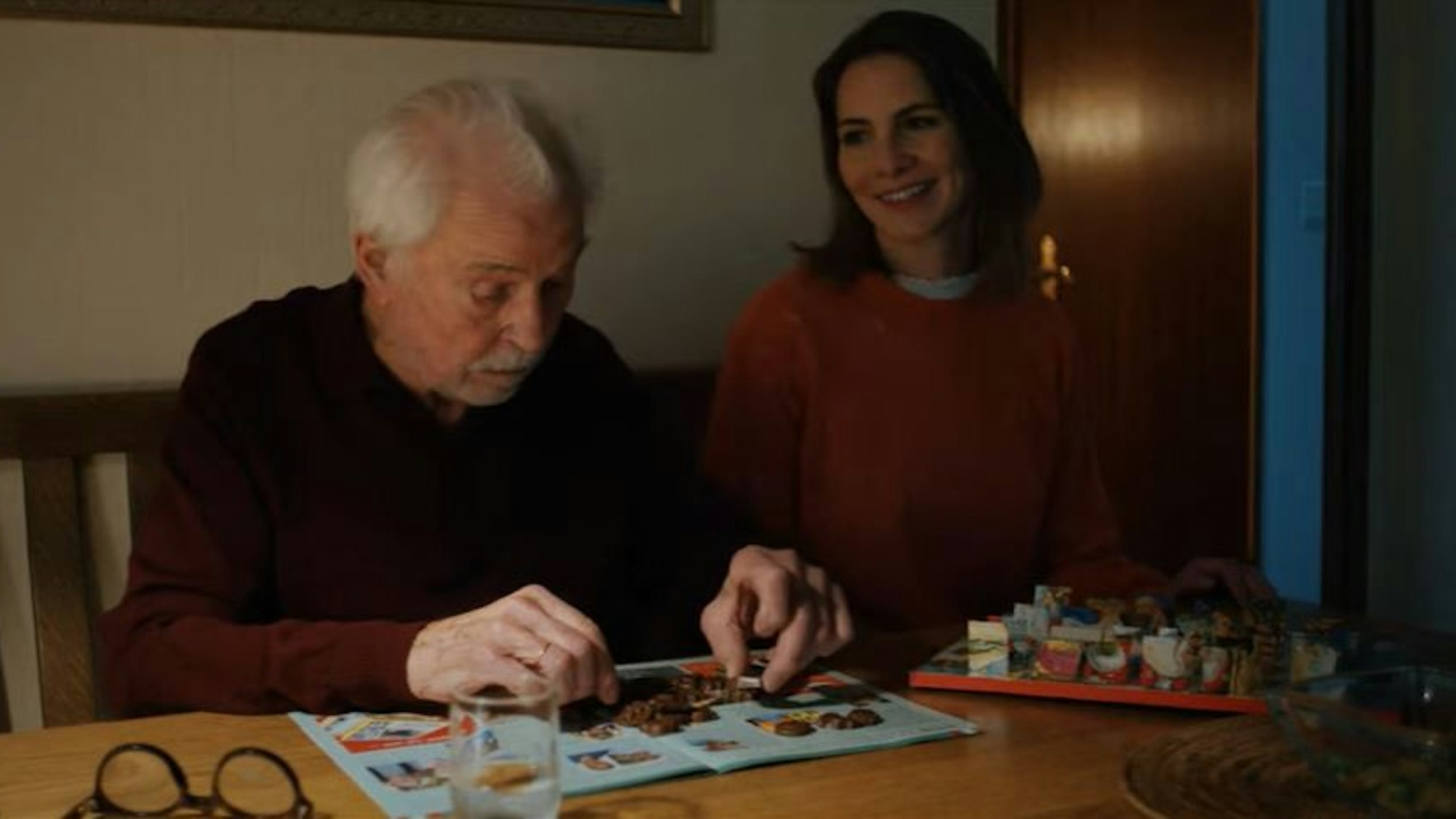 Ein älterer Mann und eine jüngere Frau sitzen an einem Tisch gemeinsam.