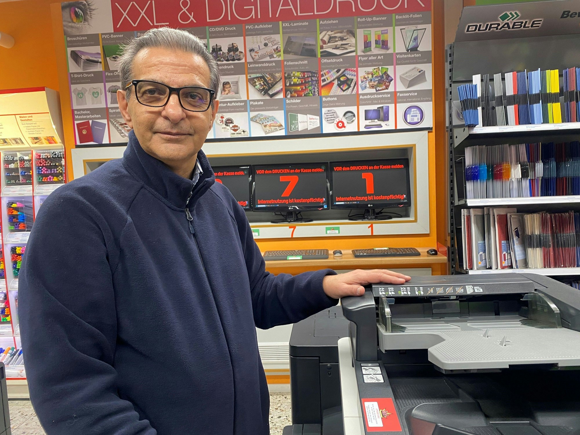 Ein Mann steht neben einem Kopiergerät und legt seine Hand drauf.