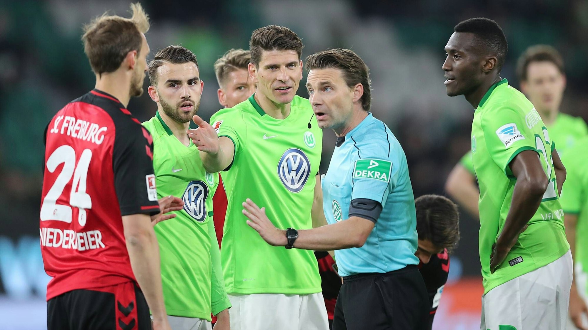 Die Spieler des VfL Wolfsburg und des SC Freiburg in einer Diskussion mit Schiedsrichter Guido Winkmann.