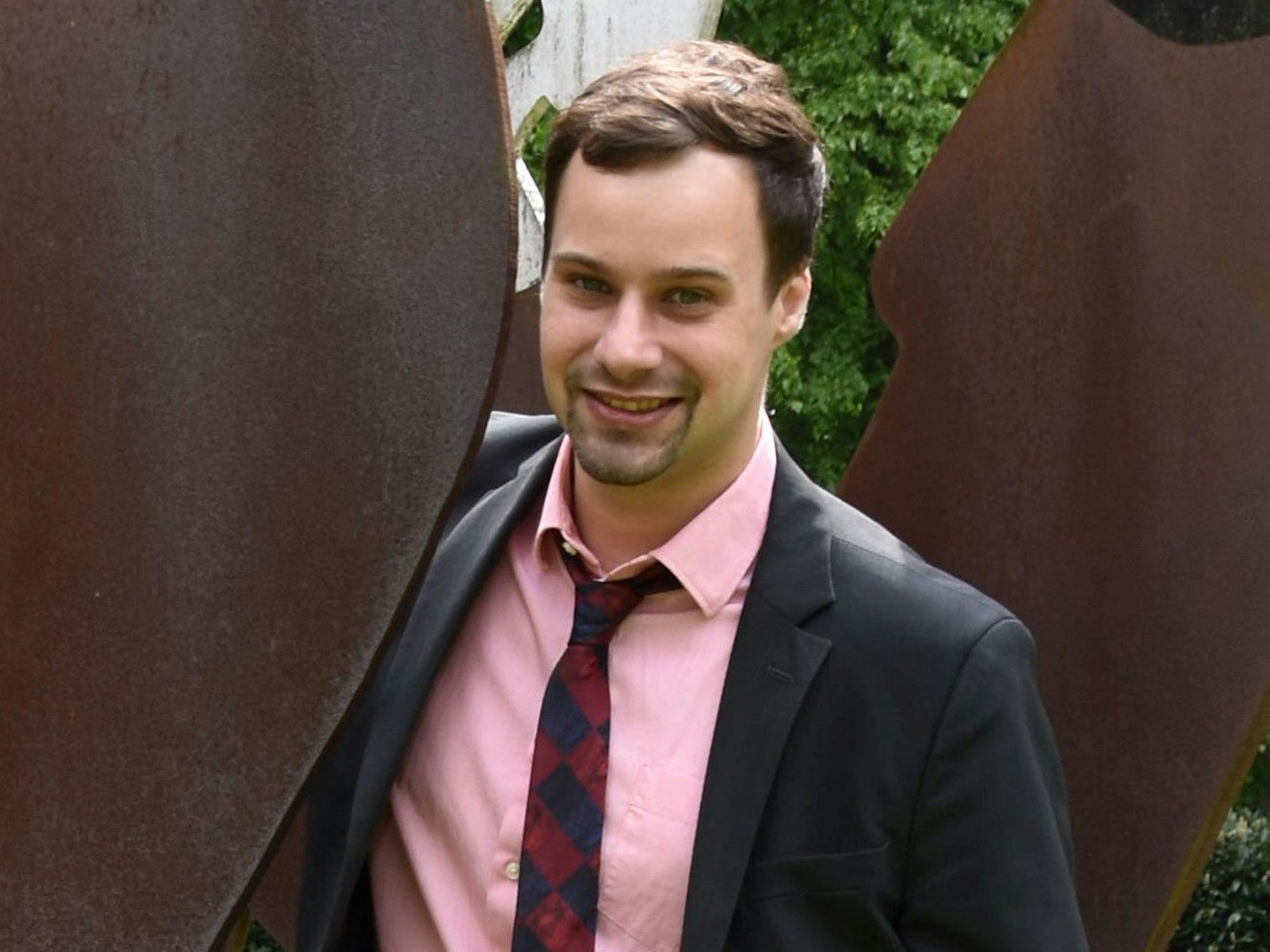 Ein Mann in einem Anzug steht neben einem Kunstwerk.