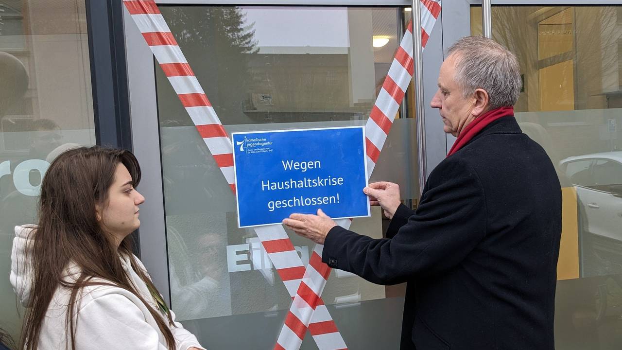 Georg Spitzley bringt ein Schild an, auf dem „Wegen Haushaltskrise geschlossen!“ steht.