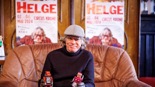 Helge Schneider hält zwei Roboter-Figuren in den Händen.