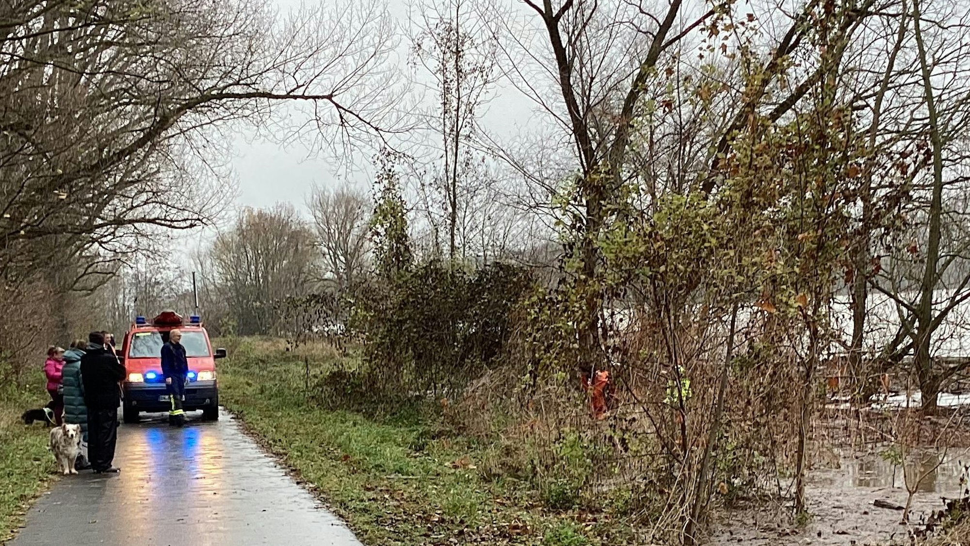 Ein Einsatzfahrzeug sowie Passanten und Passantinnen stehen am Rheinufer.