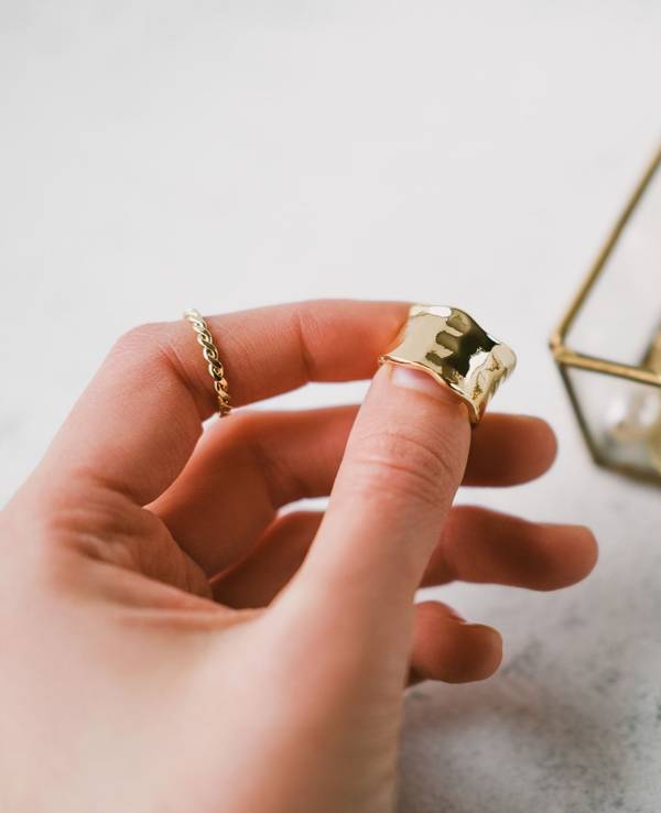 A woman's hand holds a gold ring on the background of a transparent jewelry box with accessories