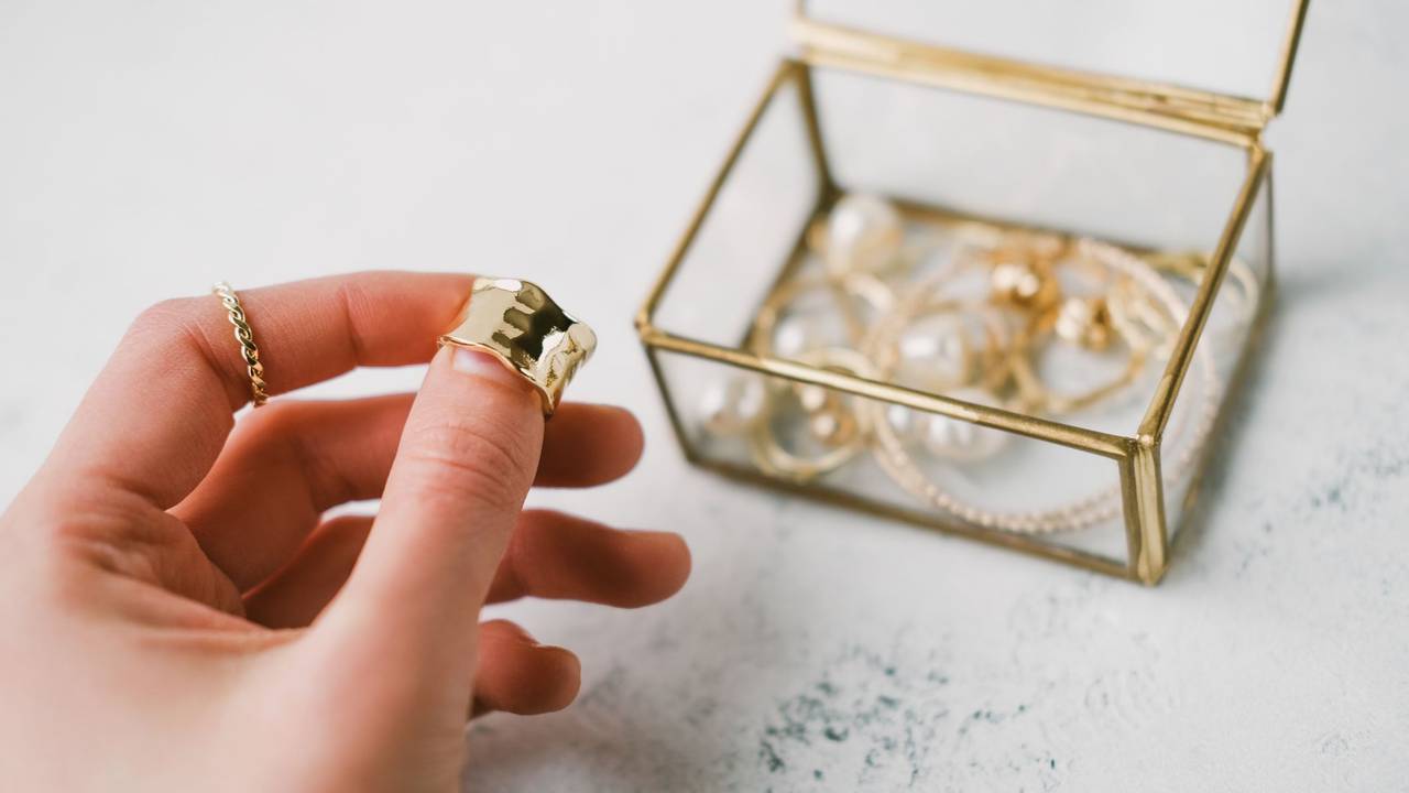 A woman's hand holds a gold ring on the background of a transparent jewelry box with accessories