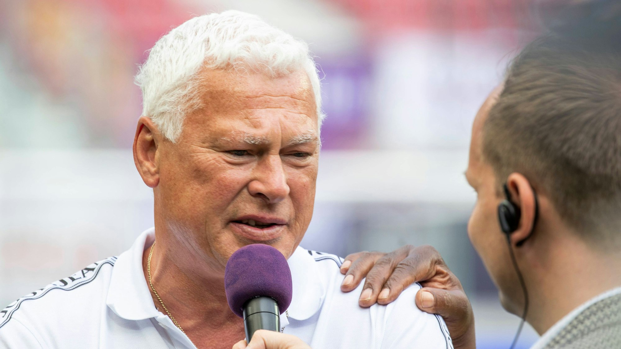Toni Polster bei einem TV-Gespräch mit Mikrofon in der Hand.