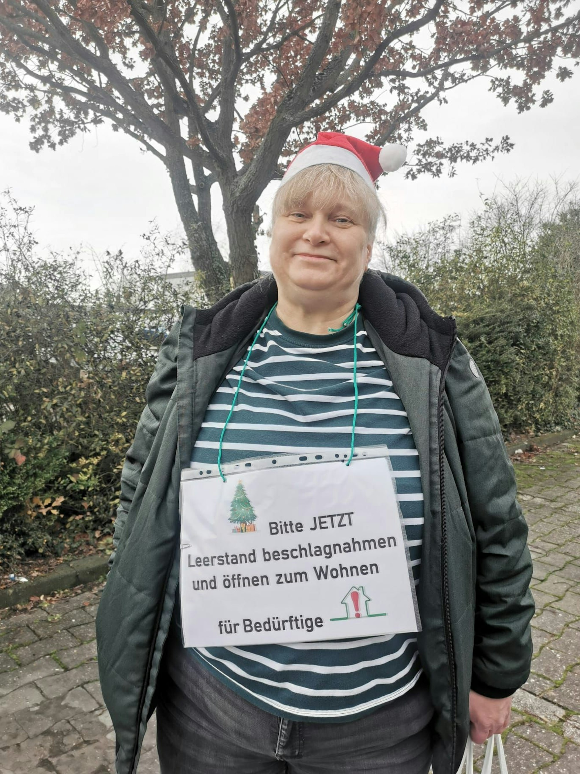Eine Frau steht mit einem Plakat um den Hals bei einer Demo.