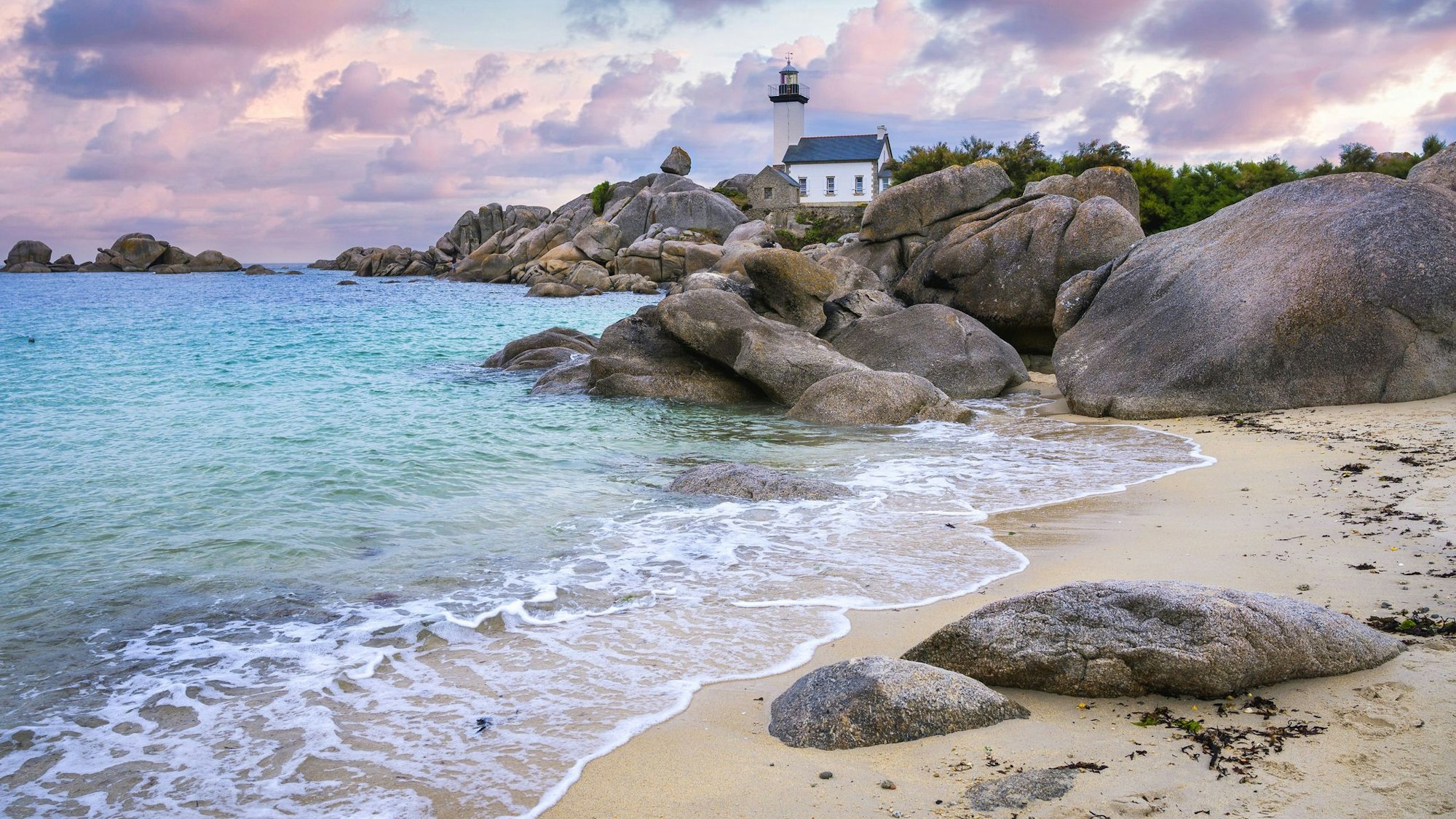 Der Leuchtturm von Pontusval, der auf einem Felsen im nördlichen Finistere in der Bretagne steht, überblickt bei Sonnenaufgang ein Meer mit transparentem, türkisfarbenem Wasser.