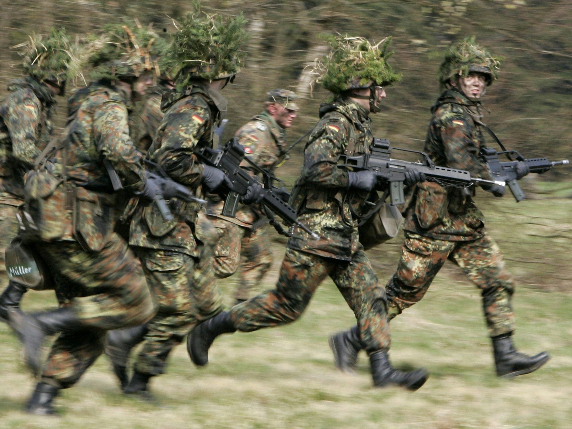 Mit Blattwerk und Gras getarnte Wehrpflichtige von den Panzergrenadieren rennen mit ihren Waffen im Rahmen ihrer Grundausbildung bei einer Übung über das freie Gelände der Knüll Kaserne in Schwarzenborn (Schwalm-Eder-Kreis).