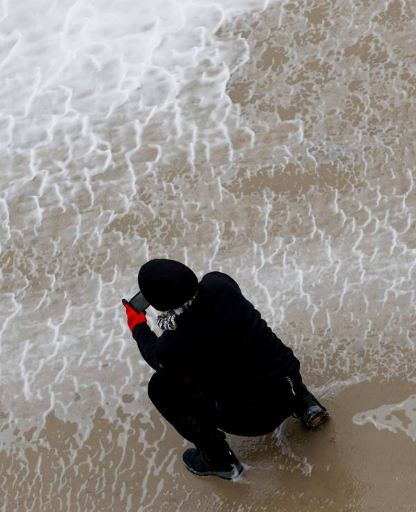 Eine Frau fotografiert mit ihrem Smartphone das von Orkanböen aufgepeitschte Wasser der Nordsee.
