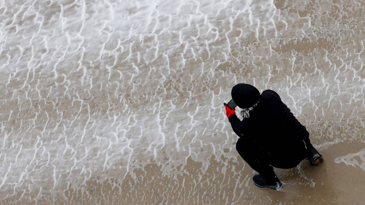 Eine Frau fotografiert mit ihrem Smartphone das von Orkanböen aufgepeitschte Wasser der Nordsee.